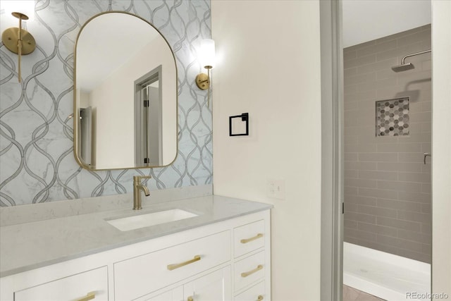 full bathroom featuring wallpapered walls, tiled shower, and vanity