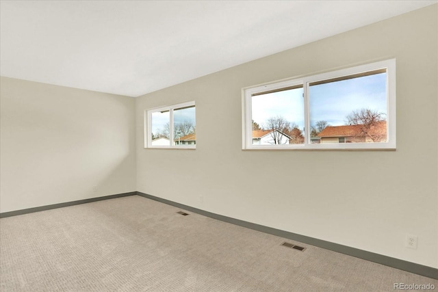 empty room featuring light carpet, visible vents, and baseboards