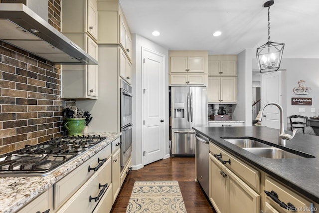 kitchen with sink, wall chimney exhaust hood, stainless steel appliances, cream cabinets, and decorative backsplash