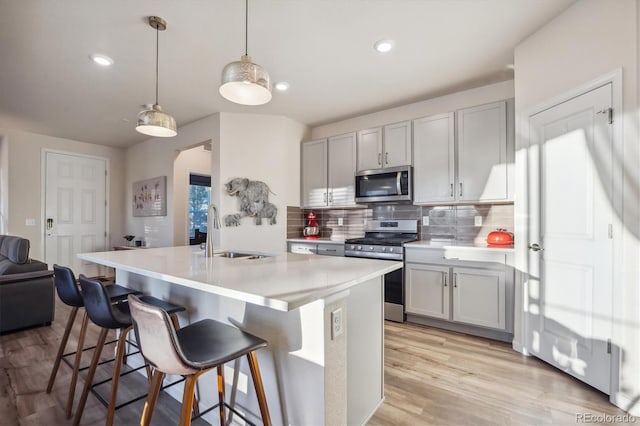 kitchen with decorative light fixtures, light wood-type flooring, stainless steel appliances, and tasteful backsplash