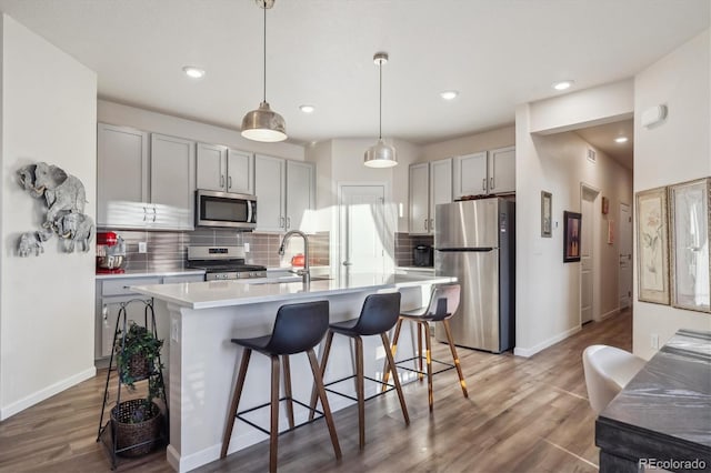 kitchen with hardwood / wood-style floors, stainless steel appliances, decorative light fixtures, and sink