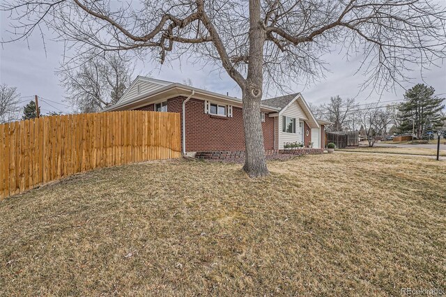 view of home's exterior with a yard, brick siding, a garage, and fence