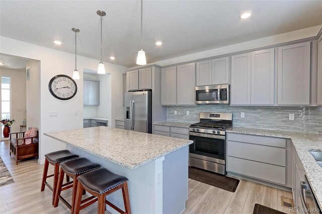 kitchen featuring gray cabinetry, a kitchen island, stainless steel appliances, and hanging light fixtures