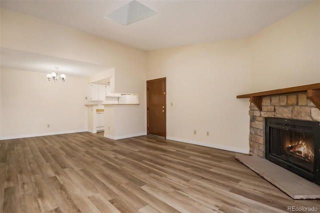 unfurnished living room featuring a stone fireplace, a notable chandelier, wood finished floors, and baseboards