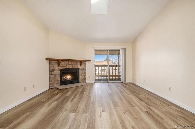 unfurnished living room with vaulted ceiling, a stone fireplace, baseboards, and wood finished floors