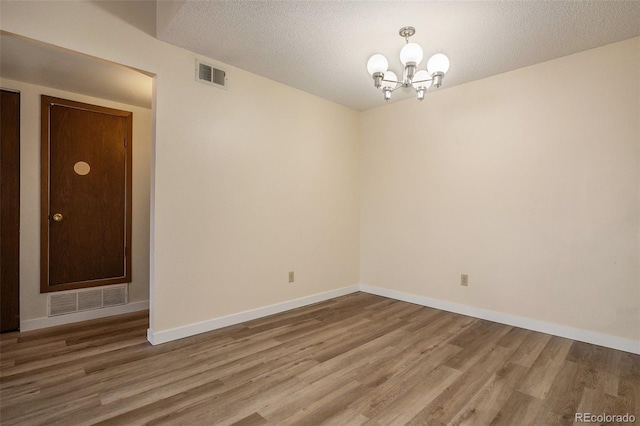 spare room featuring a notable chandelier, wood finished floors, and visible vents