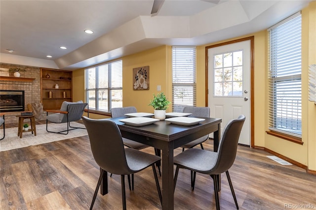 dining area featuring wood-type flooring, a brick fireplace, and built in features