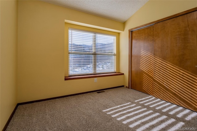 unfurnished bedroom featuring a closet, lofted ceiling, carpet flooring, and a textured ceiling