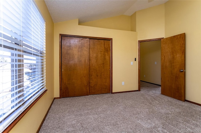 unfurnished bedroom with lofted ceiling, light carpet, a closet, and a textured ceiling