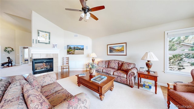 living area featuring a ceiling fan, a tiled fireplace, wood finished floors, baseboards, and high vaulted ceiling