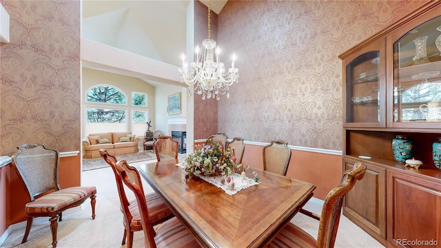 carpeted dining room with high vaulted ceiling, baseboards, wallpapered walls, and a chandelier