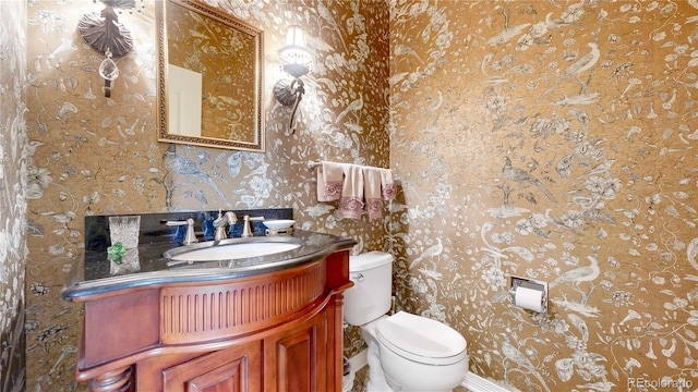 half bathroom with toilet, wallpapered walls, and vanity