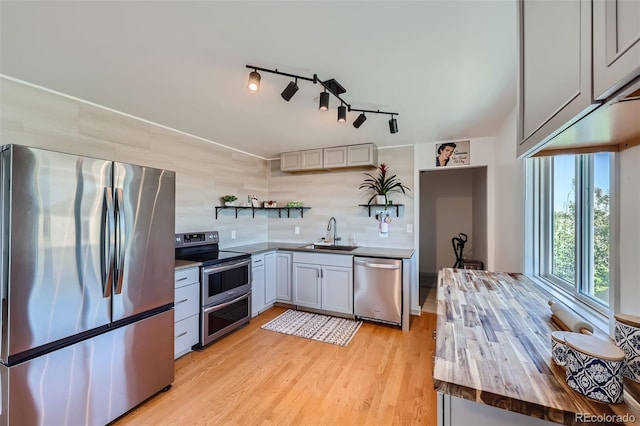 kitchen featuring open shelves, butcher block counters, light wood-type flooring, a sink, and stainless steel appliances