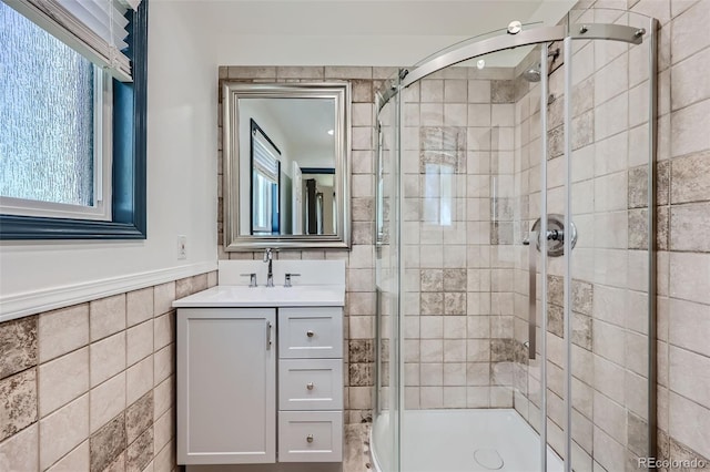 full bathroom with tile walls, a shower stall, a wainscoted wall, and vanity