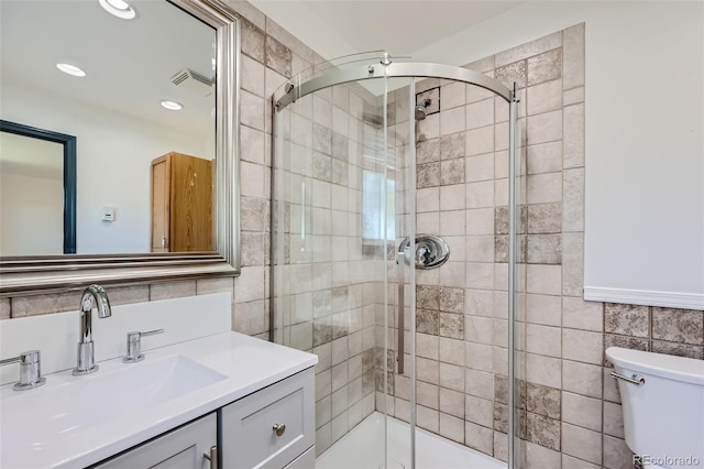 bathroom with vanity, toilet, tile walls, visible vents, and a stall shower