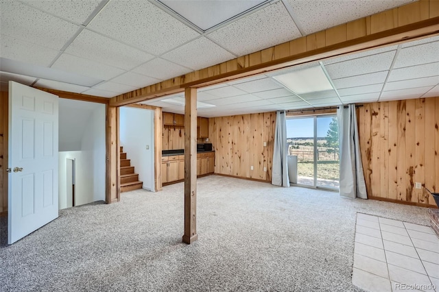 basement with wooden walls, stairway, a drop ceiling, and light carpet