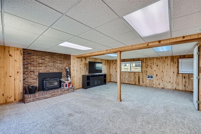 basement featuring light carpet, a brick fireplace, wood walls, and a paneled ceiling