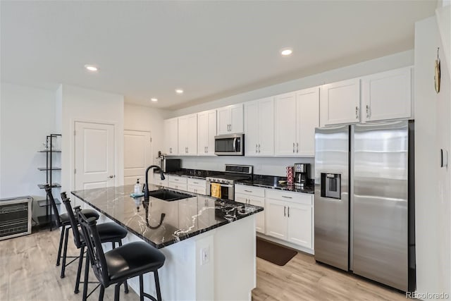 kitchen featuring white cabinets, an island with sink, appliances with stainless steel finishes, and light hardwood / wood-style flooring