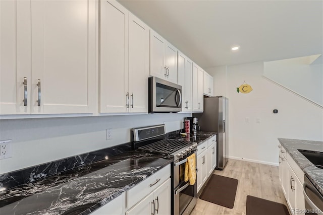 kitchen featuring dark stone counters, stainless steel appliances, white cabinetry, and light wood-type flooring