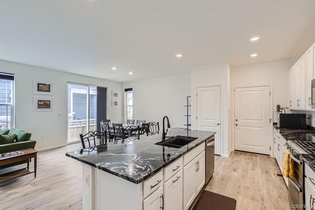 kitchen with an island with sink, sink, light hardwood / wood-style flooring, white cabinetry, and dark stone counters