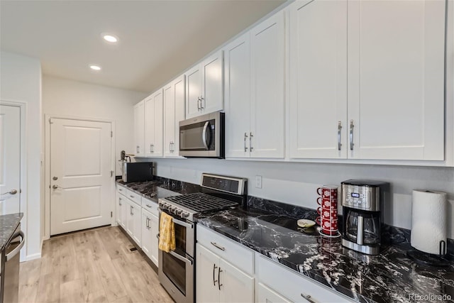 kitchen featuring white cabinets, appliances with stainless steel finishes, light hardwood / wood-style floors, and dark stone counters