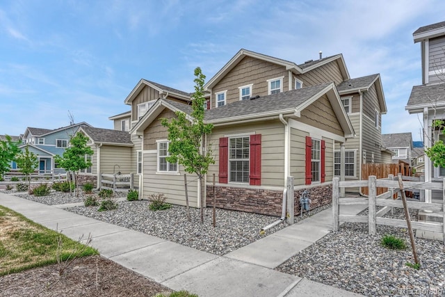 bungalow-style home featuring stone siding, roof with shingles, and fence