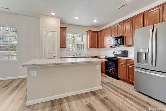 kitchen featuring black appliances, a center island, decorative backsplash, and light hardwood / wood-style flooring