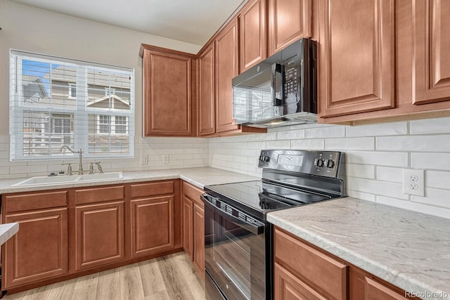 kitchen featuring light stone countertops, light hardwood / wood-style floors, sink, black appliances, and decorative backsplash