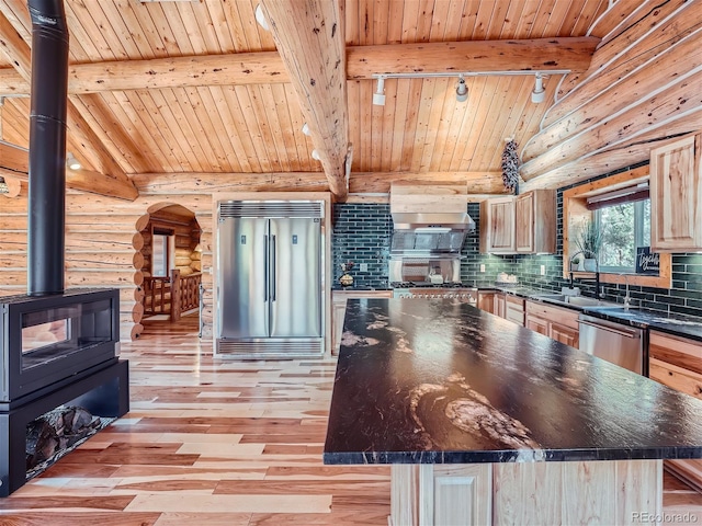 kitchen featuring built in appliances, light brown cabinetry, a kitchen island, and a wood stove