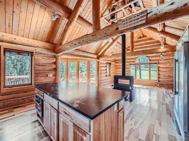 kitchen featuring beam ceiling, a center island, light brown cabinetry, high end refrigerator, and a wood stove