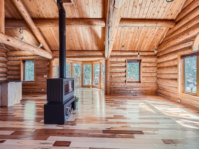 unfurnished living room with beam ceiling, wood-type flooring, a wealth of natural light, and a wood stove