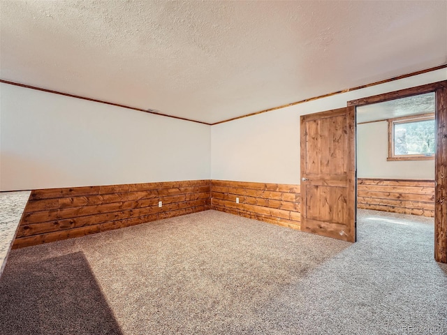 carpeted empty room with ornamental molding, wooden walls, and a textured ceiling