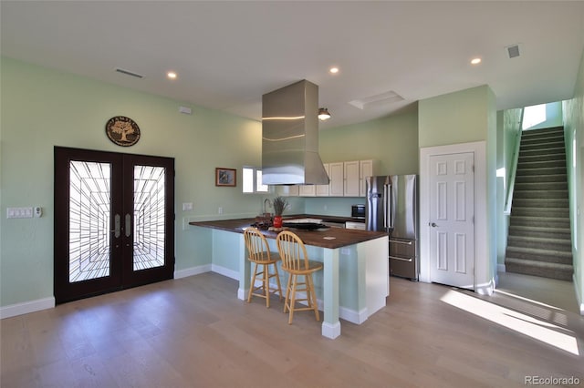 kitchen with french doors, wall chimney range hood, kitchen peninsula, a breakfast bar area, and high quality fridge
