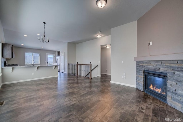 unfurnished living room featuring sink, a notable chandelier, a stone fireplace, and dark hardwood / wood-style flooring