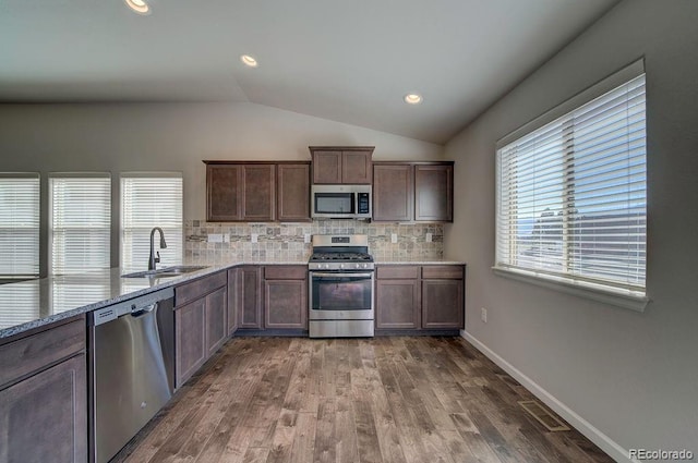 kitchen featuring dark hardwood / wood-style flooring, backsplash, vaulted ceiling, sink, and stainless steel appliances