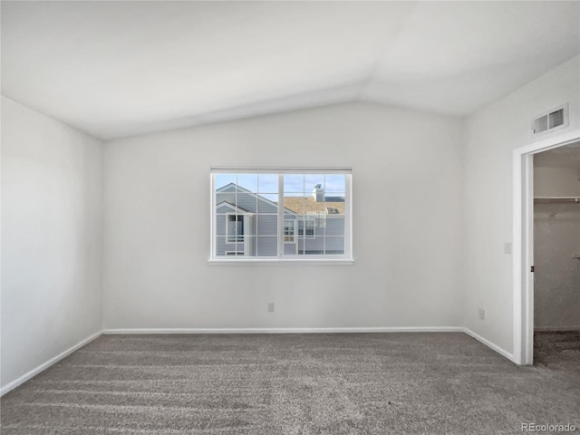 unfurnished bedroom with dark colored carpet, a closet, a walk in closet, and vaulted ceiling