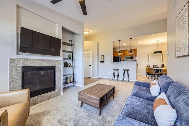 carpeted living room with built in shelves, a tiled fireplace, and ceiling fan