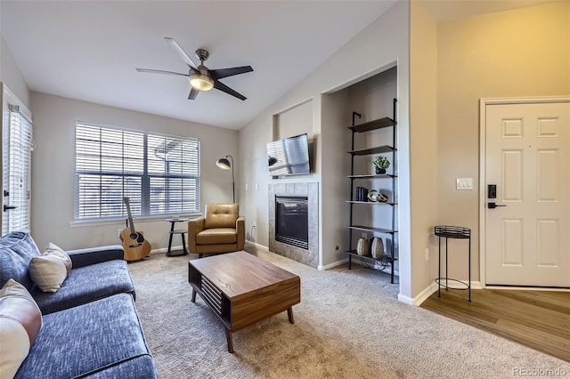 living room with vaulted ceiling, ceiling fan, a tiled fireplace, carpet, and built in shelves