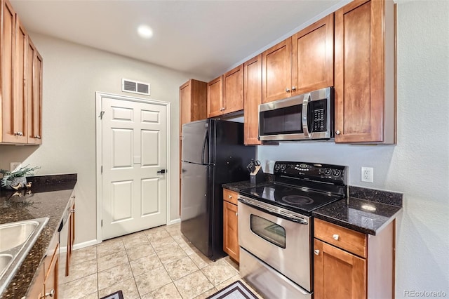 kitchen featuring sink, dark stone countertops, stainless steel appliances, and light tile patterned flooring