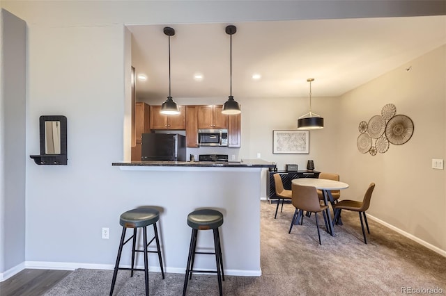 kitchen featuring pendant lighting, range, black fridge, kitchen peninsula, and a breakfast bar