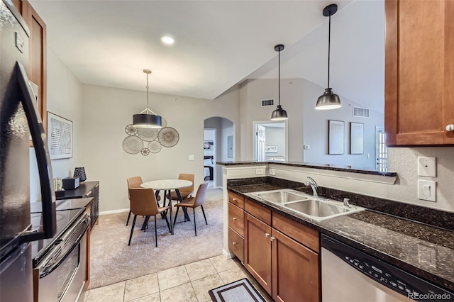 kitchen with dark stone counters, hanging light fixtures, light carpet, sink, and stainless steel appliances