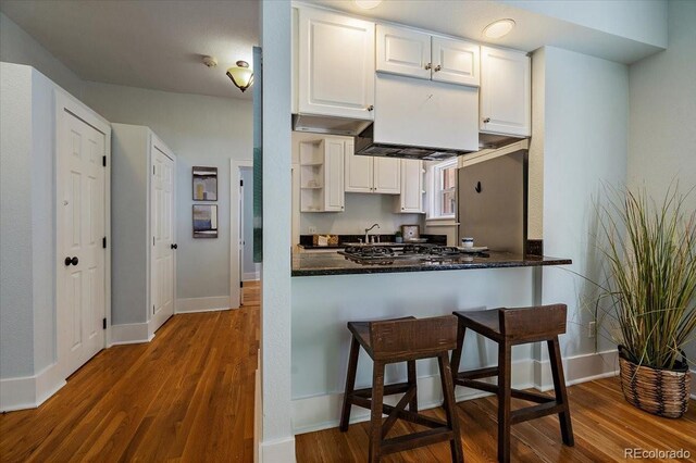 kitchen with kitchen peninsula, dark stone countertops, wood-type flooring, and white cabinets