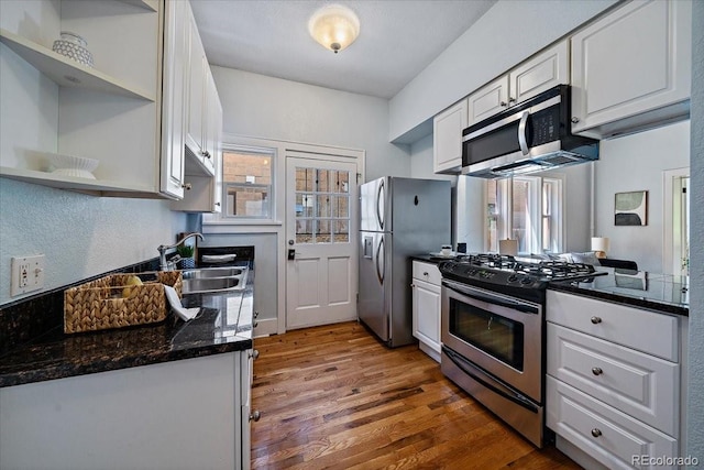 kitchen with hardwood / wood-style floors, white cabinets, dark stone countertops, sink, and appliances with stainless steel finishes