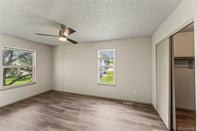 1344 Firefly Cir, Colorado Springs, CO 80916 - unfurnished bedroom featuring multiple windows, light wood finished floors, a closet, and a textured ceiling