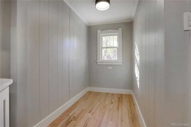 unfurnished room featuring wooden walls, ornamental molding, and light wood-type flooring