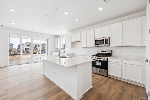 6636 N Nepal St, Aurora, CO 80019 - kitchen featuring appliances with stainless steel finishes, a sink, light wood finished floors, a kitchen island with sink, and white cabinets