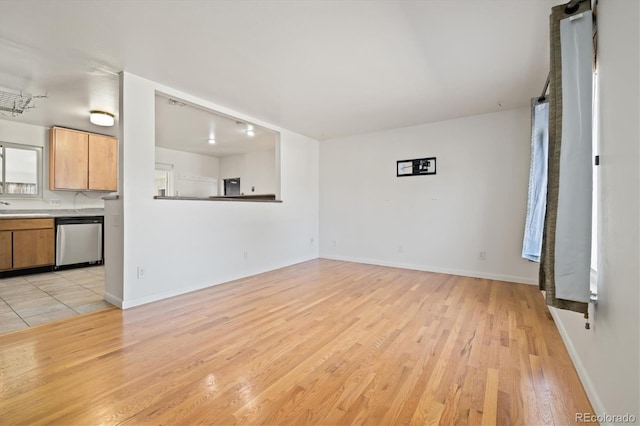 unfurnished living room featuring a sink, light wood-type flooring, baseboards, and a barn door