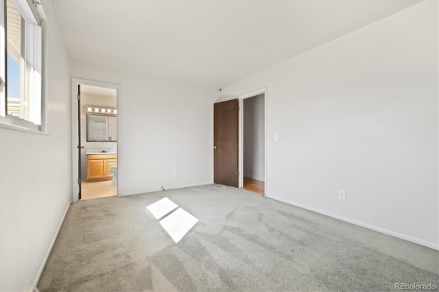 unfurnished bedroom with light colored carpet, ensuite bathroom, and baseboards