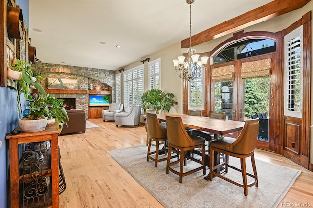 dining space with a notable chandelier, a fireplace, french doors, and light wood-type flooring