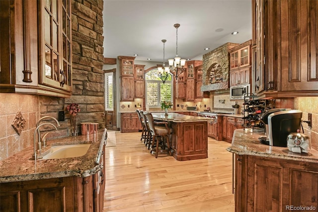 kitchen with stone countertops, stainless steel microwave, sink, hanging light fixtures, and a center island